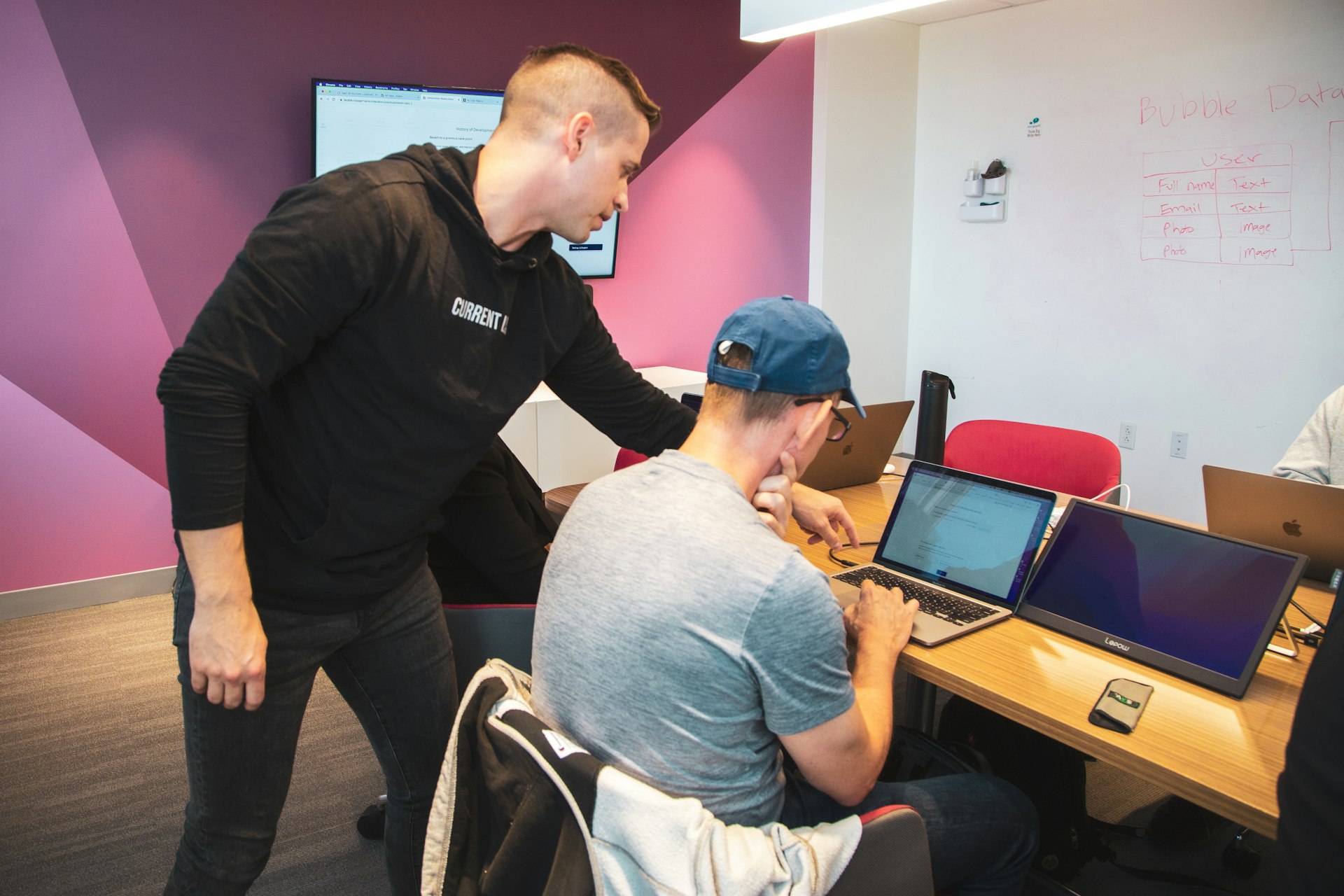 Two colleagues working from one laptop at a shared desk.
