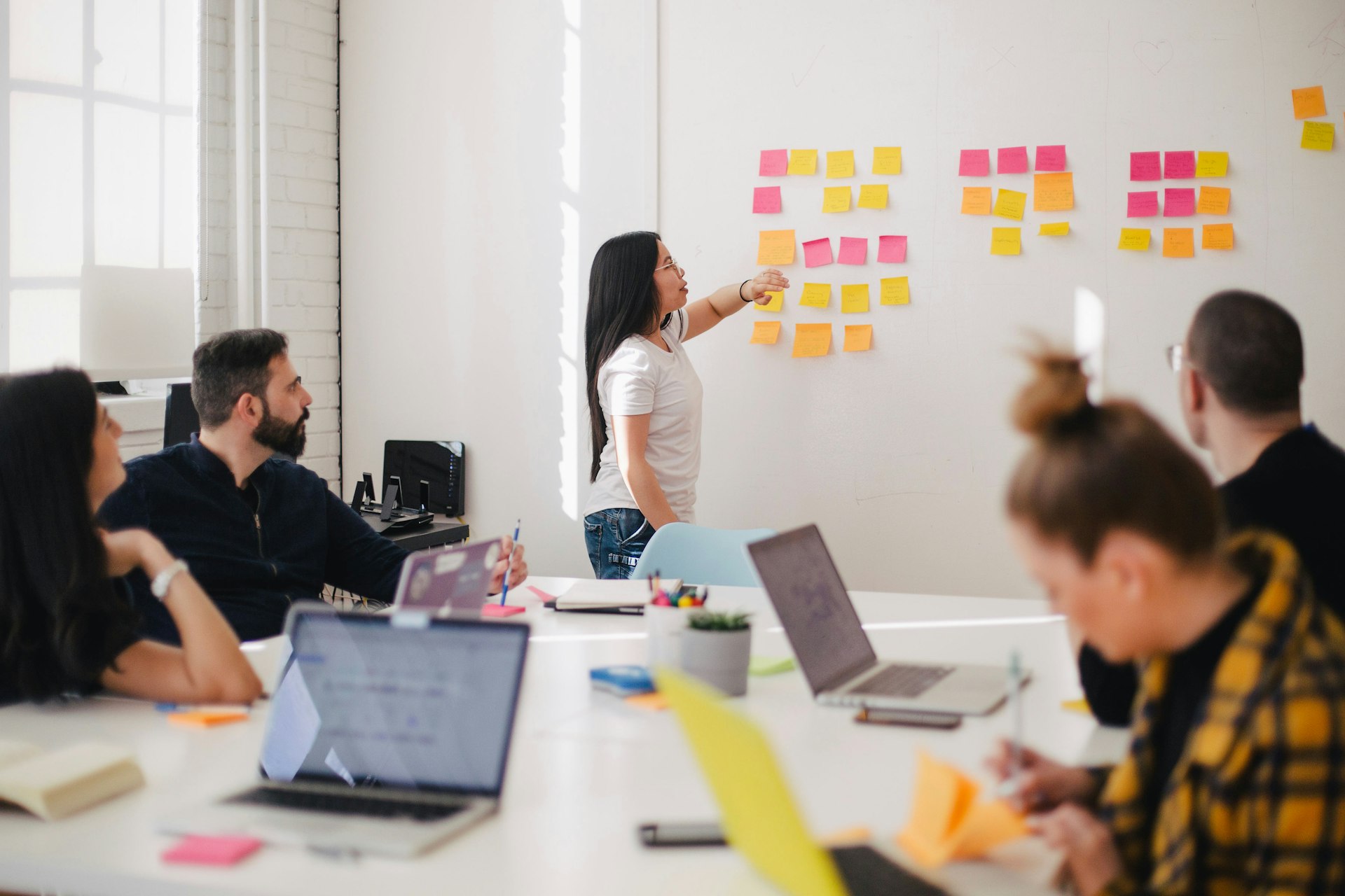 A team meeting around a shared table, one member working through notes on a wall.